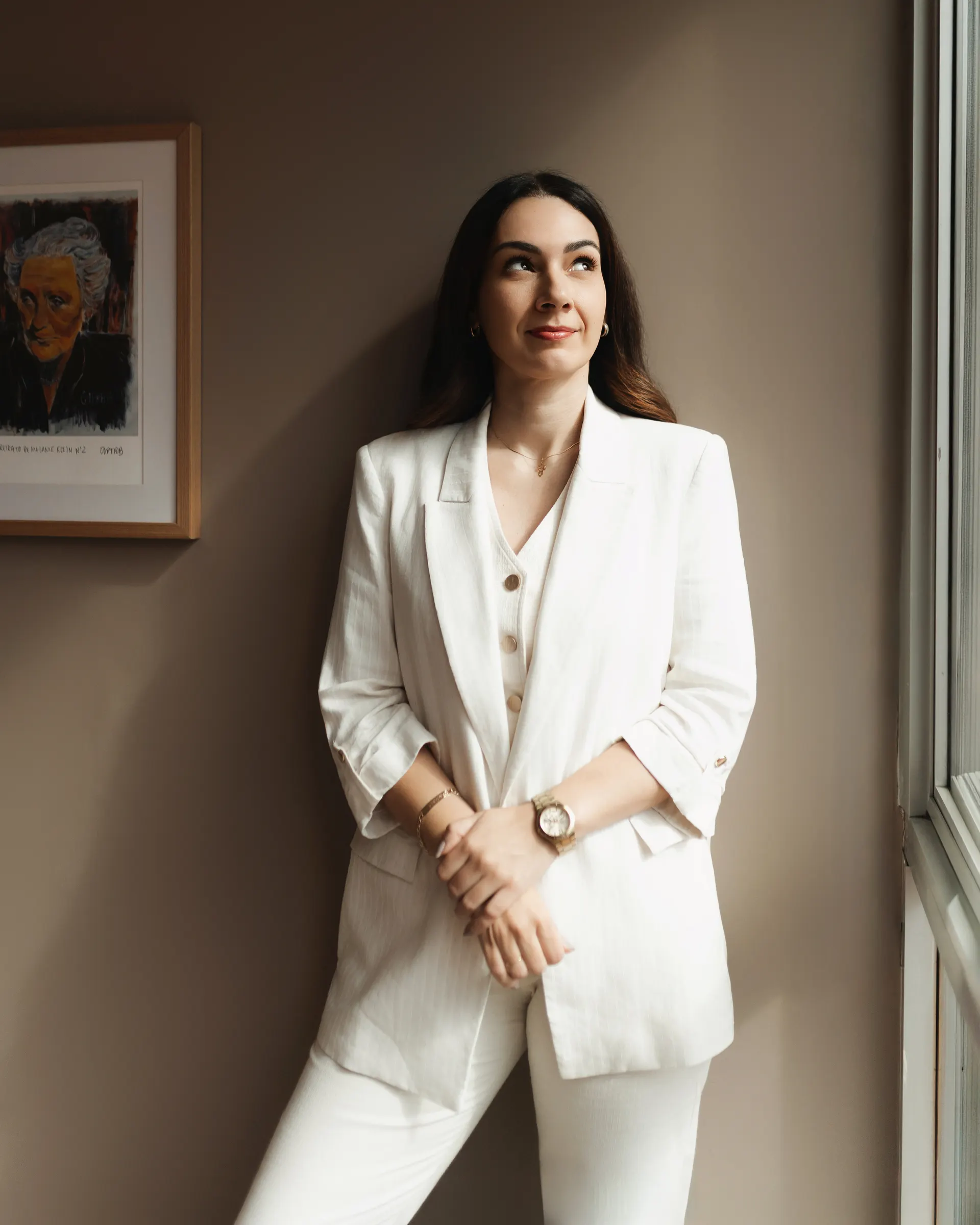 Gabriela Vargas de pé, de blazer branco, olhando para o alto