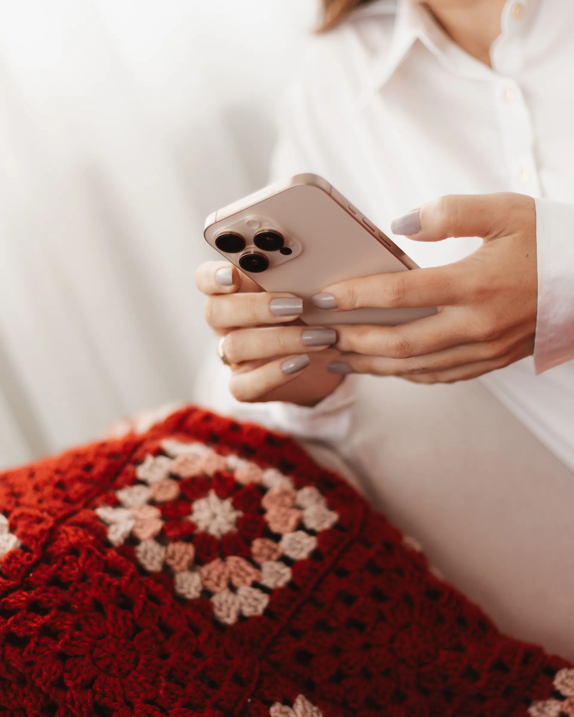 Mãos segurando um celular, sobre uma manta de crochê vermelha