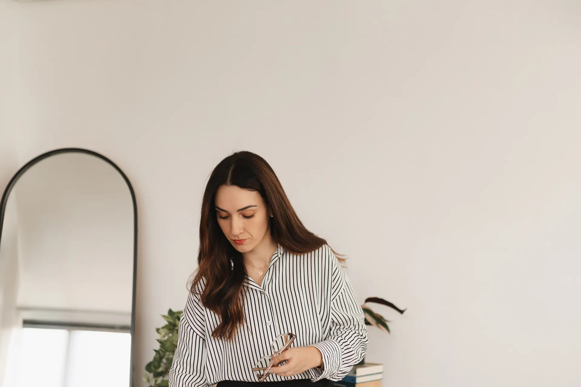 Gabriela Vargas num escritório claro, de camisa listrada, segurando os óculos